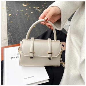Detail view of beige Saffiano mini handbag with gold clasp and chain strap held by model