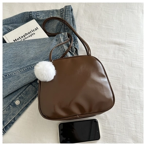 Détail d'un sac à bandoulière en similicuir marron brillant avec pompon blanc doux