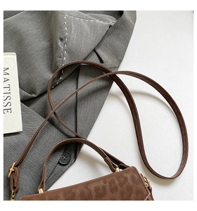 Close-up of brown leopard-patterned suede crossbody bag with metal buckle and strap details