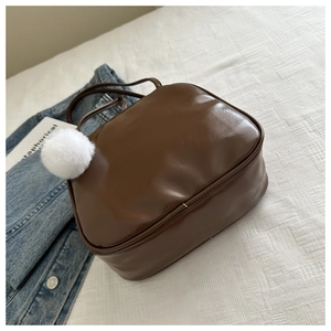 Détail du sac polochon en similicuir marron foncé avec pompon blanc et bandoulière fine
