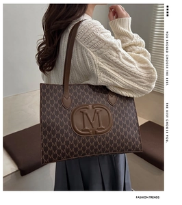 Close-up of a brown monogram tote bag with embossed M logo and adjustable shoulder strap