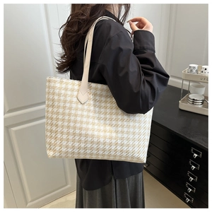 Close-up of houndstooth tote bag with beige leather straps worn by a model in interior