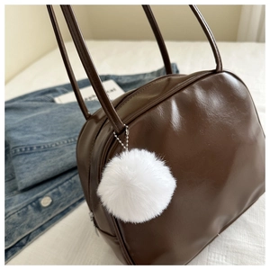 Détail du sac bandoulière marron brillant avec pompon blanc sur fond en denim bleu