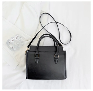 Dettaglio borsa a mano nera con finiture dorate su sfondo di un elegante abito bianco
