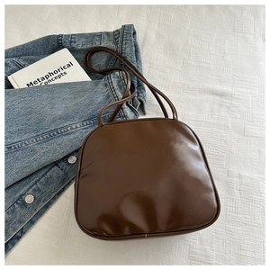 Gros plan du sac boston en cuir marron brillant sur veste en jean et drap blanc texturé