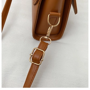 Détail du sac à bandoulière en cuir marron avec boucle dorée et bandoulière réglable