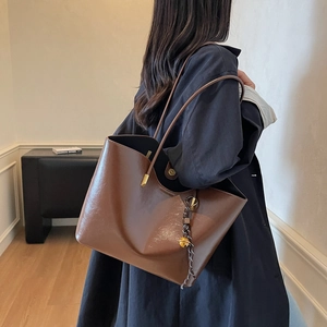 Brown leather tote bag with gold bell charm and shoulder strap shown in a lifestyle scene