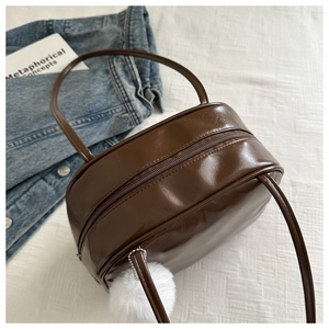 Détail d'un sac à bandoulière en cuir marron foncé brillant avec un pompon blanc pelucheux