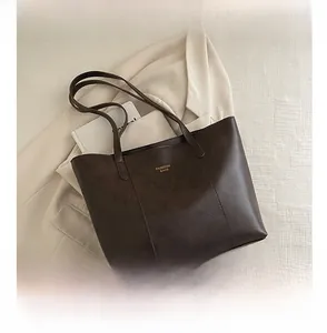 Flat lay of brown leather tote bag with gold logo next to a phone for size comparison