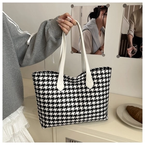 Close-up of classic black and white houndstooth tote bag with leather handles in a chic setting