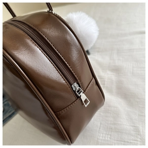 Détail du sac à main marron en cuir PU avec fermeture éclair argentée et pompon en fourrure