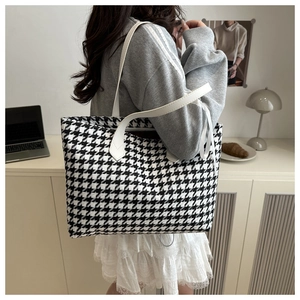 Detail of black and white houndstooth tote bag with a white ribbon bow and leather strap