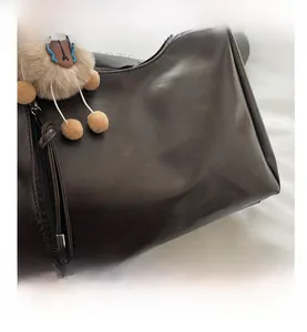 Close-up of dark brown matte leather shoulder bag with zipper and plush doll charm