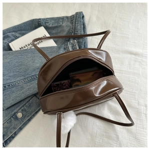 Vue de dessus du sac à main en cuir verni marron foncé avec pompon blanc et fermeture éclair