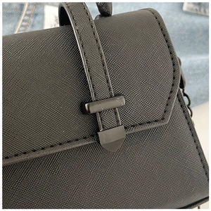 Detail of black Saffiano texture leather handbag with matte metal buckle and chain strap