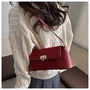 Detail of red leather shoulder bag with silver buckle worn by a model in a minimal setting