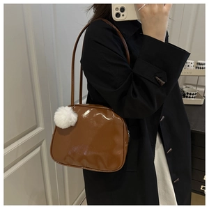 Sac à bandoulière marron brillant avec pompon blanc duveteux porté par le mannequin