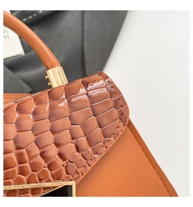 Detail of orange-brown crossbody bag showing embossed crocodile texture and gold buckle