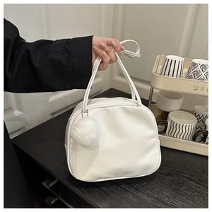 Gros plan d'un sac à main blanc minimaliste avec pompon en peluche et poignée supérieure