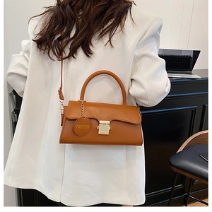 Détail d'un sac porté épaule en cuir marron avec boucle dorée et breloque sur blazer blanc