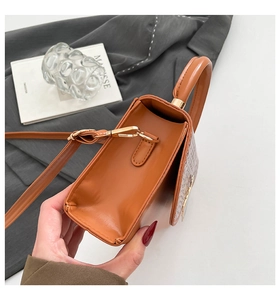 Close-up of brown textured flap handbag with gold metal clasp and top handle detail
