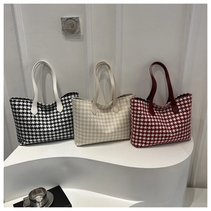 Three houndstooth pattern tote bags in black, beige, and red on a modern display stand