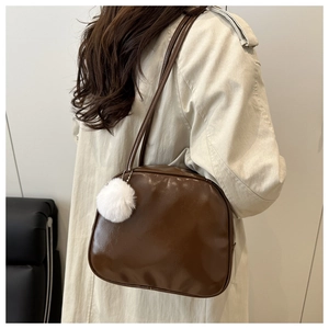 Sac à main vintage marron avec breloque boule en peluche blanche porté à l'épaule