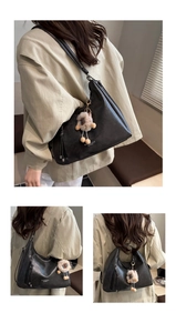 Detail of black leather hobo bag with plush brown charm and long adjustable strap
