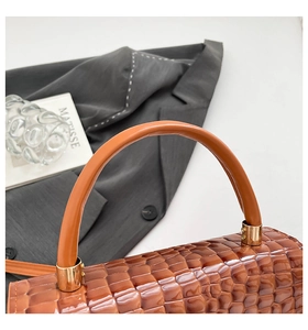 Detail of glossy brown crocodile embossed texture and round handle with gold hardware