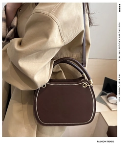 Detail of a dark brown crossbody bag with gold accents shown in an indoor office setting