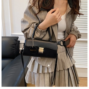 Vue détaillée d'un sac à bandoulière noir avec boucle dorée et breloque sur mannequin