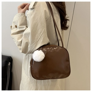 Brown leather shoulder bag with white plush charm shown on a beige trench coat