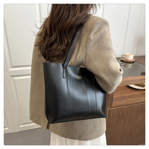 Detail of black textured leather tote bag featuring gold lettering and long handles