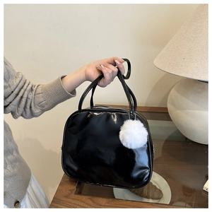 Vue détaillée d'un sac à main en cuir verni noir avec un charmant pompon blanc