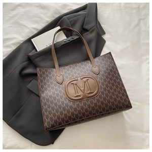 Detailed macro view of the brown monogram tote bag featuring embossed M letter logo and texture