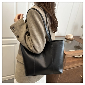 Side view of black PU leather tote bag worn by a model in a cozy indoor setting