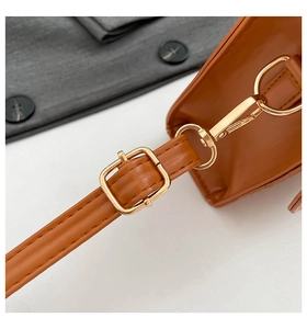 Close-up of brown leather bag strap with gold metal buckle and detailed stitching