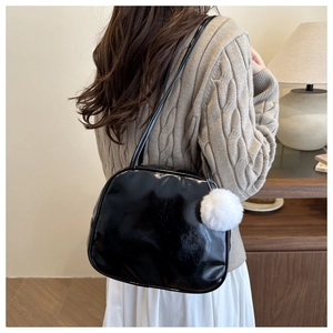 Sac bandoulière en cuir verni noir avec un petit pompon blanc décoratif en détail