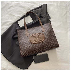 Detail of vintage brown leather tote bag with M letter pattern on black blazer