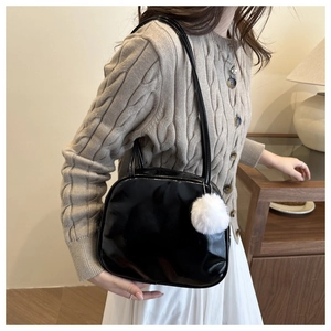 Close-up of black patent leather shoulder bag with a white fuzzy pompom charm