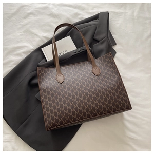 Vue de dessus d'un grand sac cabas marron avec motif monogramme M sur tissu texturé blanc