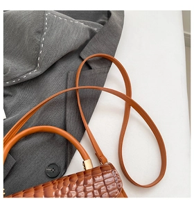 Detailed macro view of brown croc-embossed leather texture and gold hardware on a handbag
