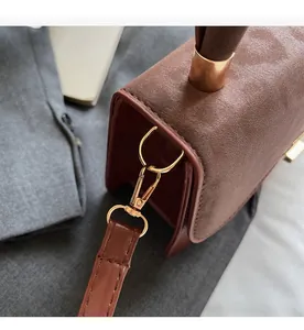 Detailed close-up of golden metal D-ring and spring hook on brown crossbody bag strap