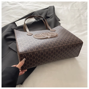 Vue détaillée du sac cabas en toile marron avec motif M et écusson en cuir