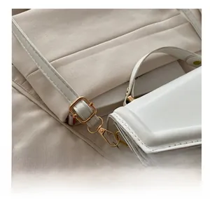 Detail der verstellbaren goldenen Metallschnalle an weißer Kunstleder-Umhängetasche