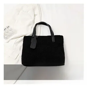 Size comparison of a black fuzzy fleece tote bag with leather straps next to a blue phone