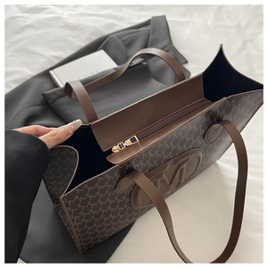 Détail d'un grand sac cabas marron avec monogramme de lettres M et logo rond en relief