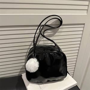 Sac bandoulière en cuir verni noir brillant avec un pompon blanc sur un livre