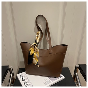 Detailed view of a brown faux leather tote bag with printed silk scarf on handle