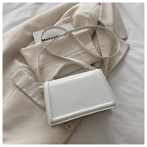 Close-up of white minimalist square crossbody bag with gold hardware on aesthetic background